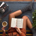 Een vrouw leest geconcentreerd een boek met een kop koffie naast haar, een beeld van rustige zelfontwikkeling op latere leeftijd