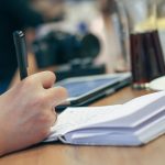 Persoon schrijft motiverende teksten in een notitieboek aan een bureau