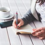 Vrouw schrijft in notitieboek aan bureau als oefening voor zelfImage opbouwen