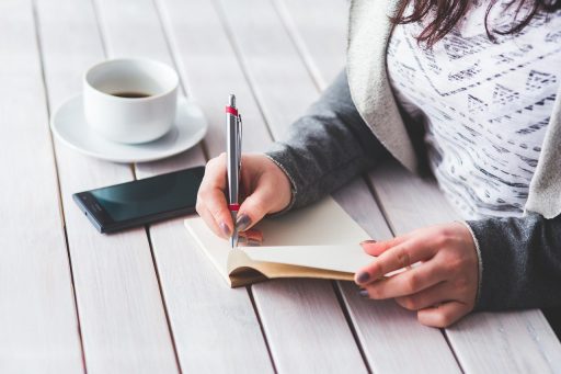 Vrouw schrijft in notitieboek aan bureau als oefening voor zelfImage opbouwen
