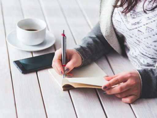 Vrouw schrijft in notitieboek aan bureau als oefening voor zelfImage opbouwen
