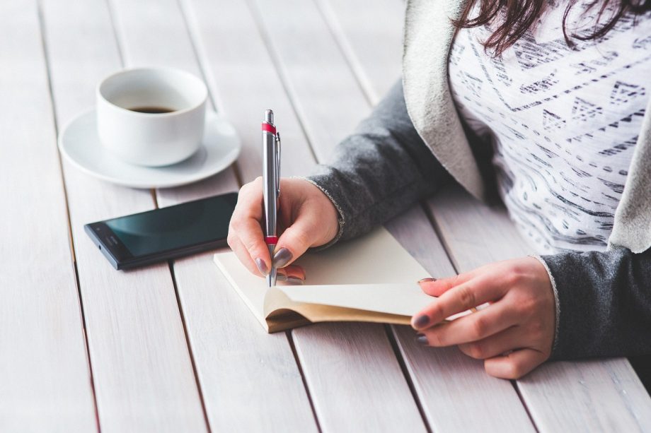 Vrouw schrijft in notitieboek aan bureau als oefening voor zelfImage opbouwen